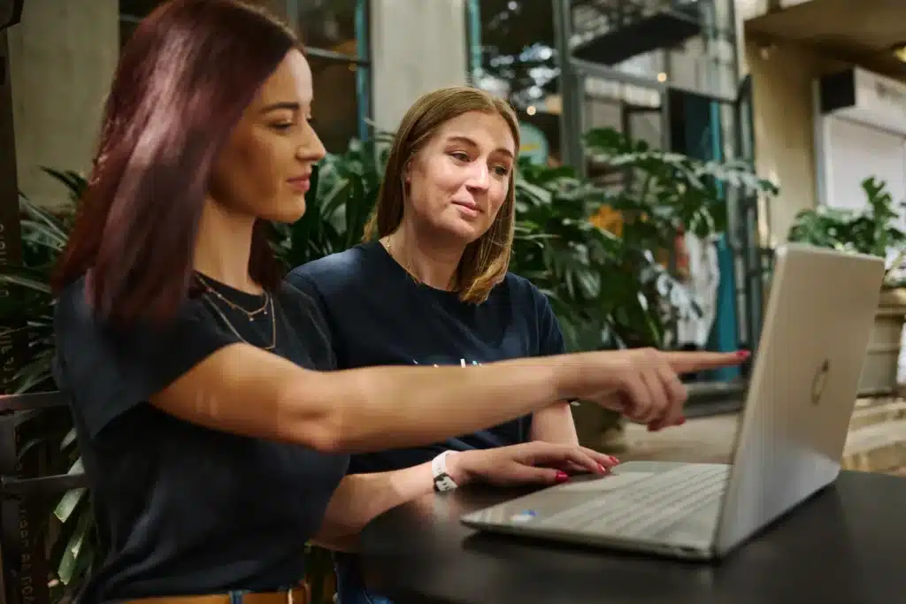 a photograph of 2 females working at a computer and one of them pointing to the screen
